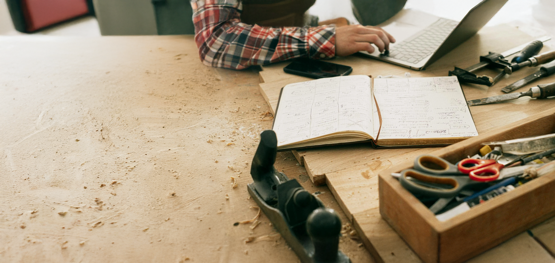 Person working on a laptop with tools and a notebook on a wooden desk